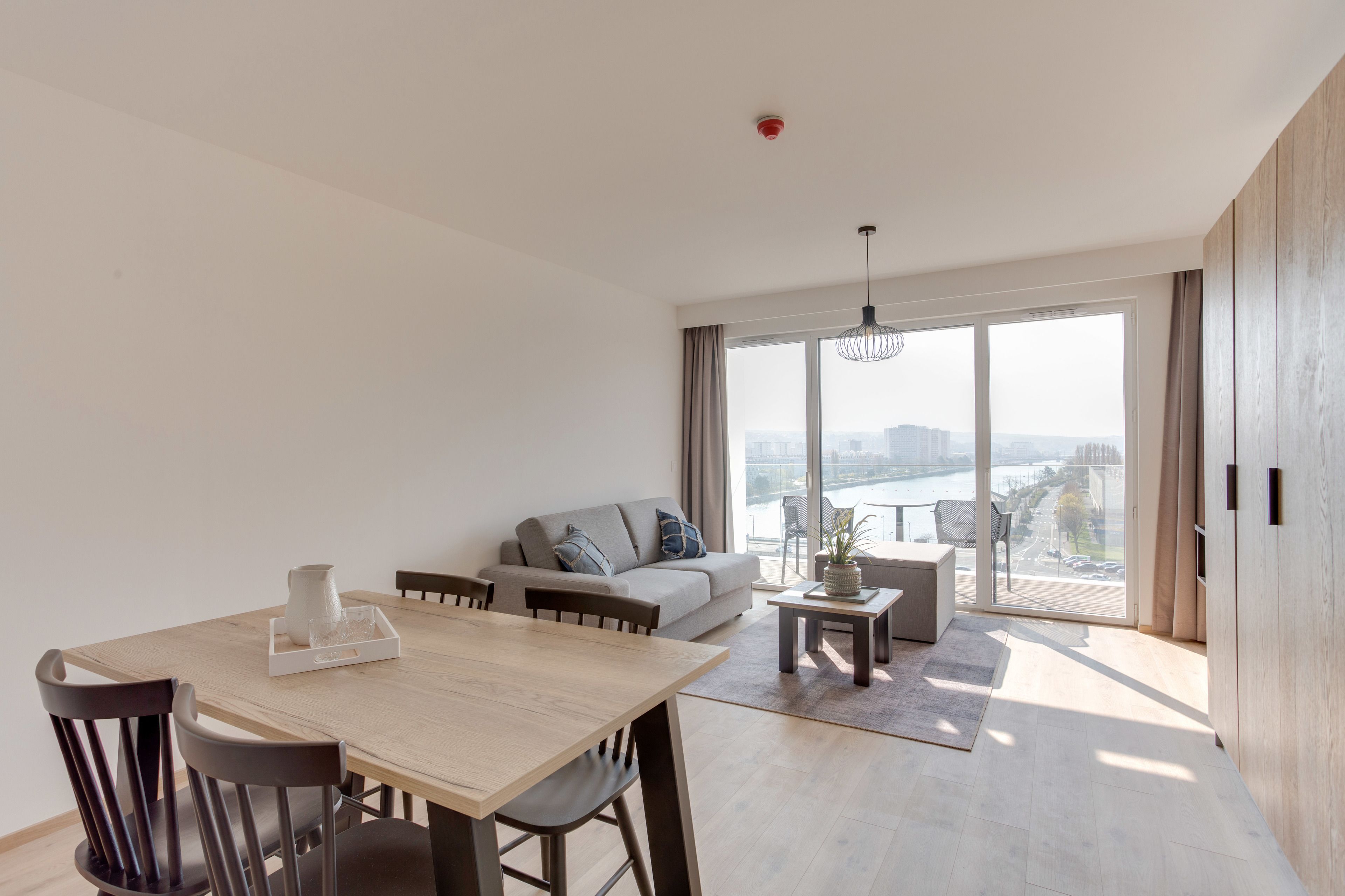 A modern living room with a dining area, large windows, and a view of a body of water.