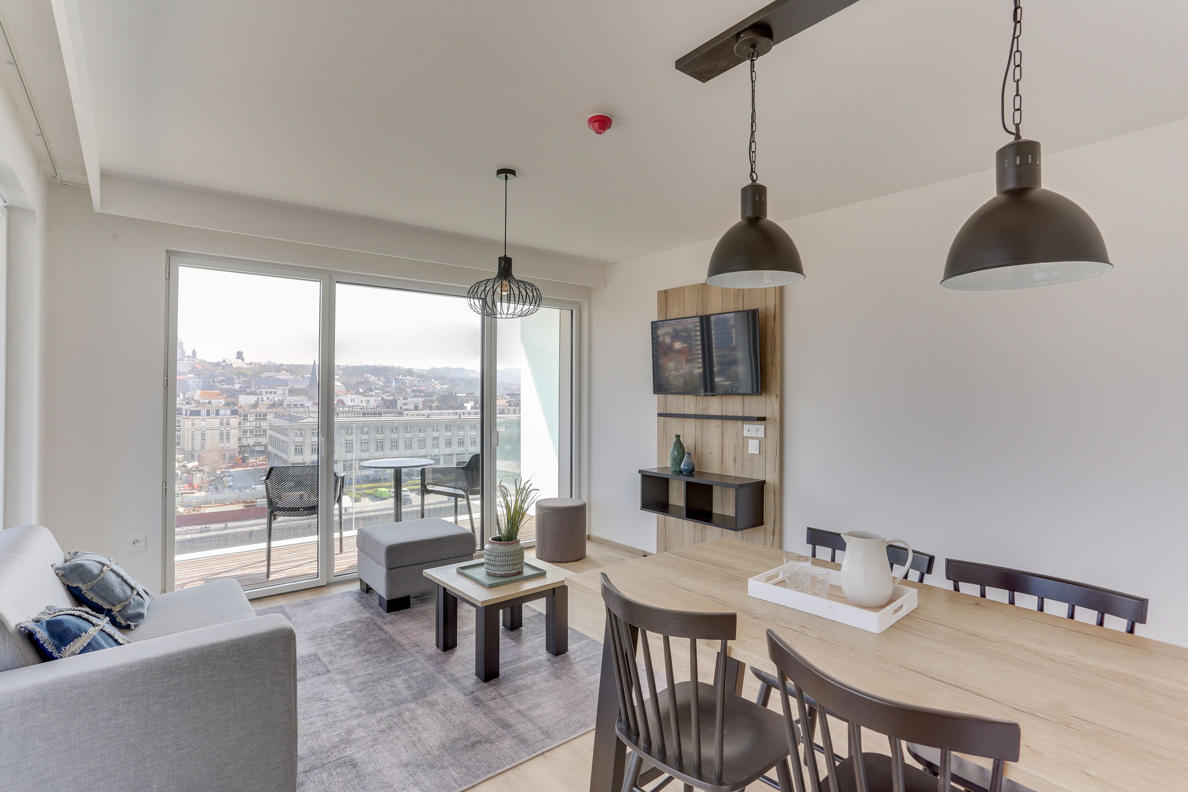 A modern living room with a dining area, large windows, and a city view.