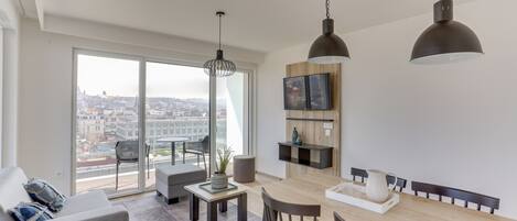 A modern living room with a dining area, large windows, and a city view.