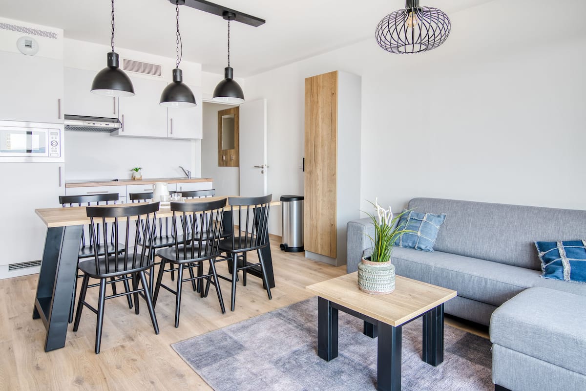 Eine moderne Küche mit Essbereich, einem grauen Sofa und einem Holztisch.