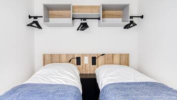 A bedroom with two beds, a wooden headboard, and a shelf above the beds with hooks.