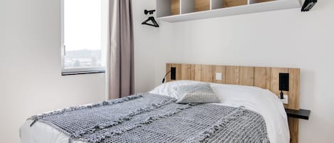 A modern bedroom with a large bed, a wooden headboard, built-in shelving, and a window with curtains.