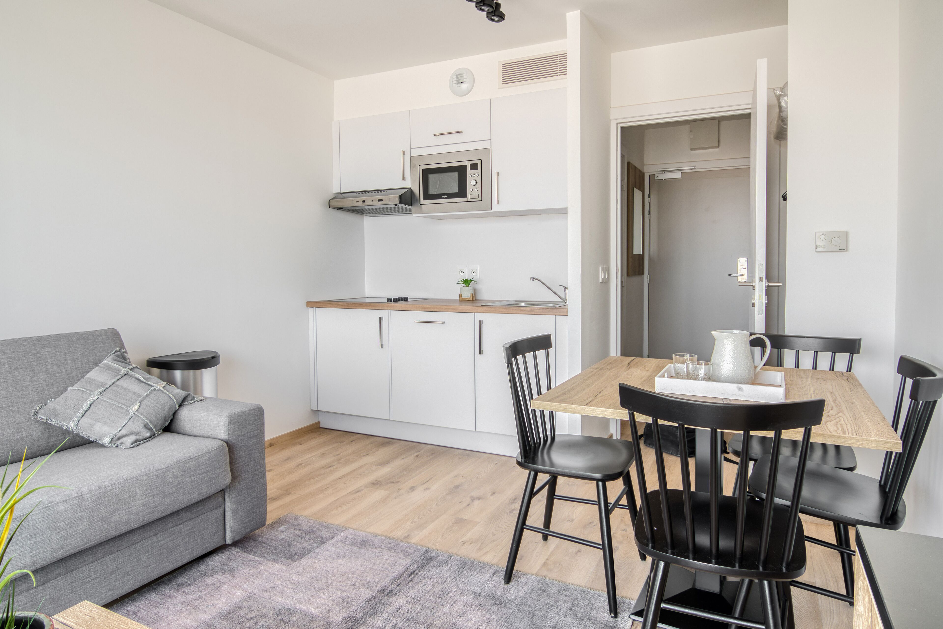 A modern kitchen with white cabinets, a microwave, and a wooden dining table with black chairs.
