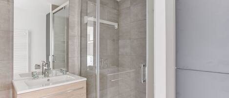 A modern bathroom with a glass shower enclosure, a white sink with a mirror, and a wooden vanity.