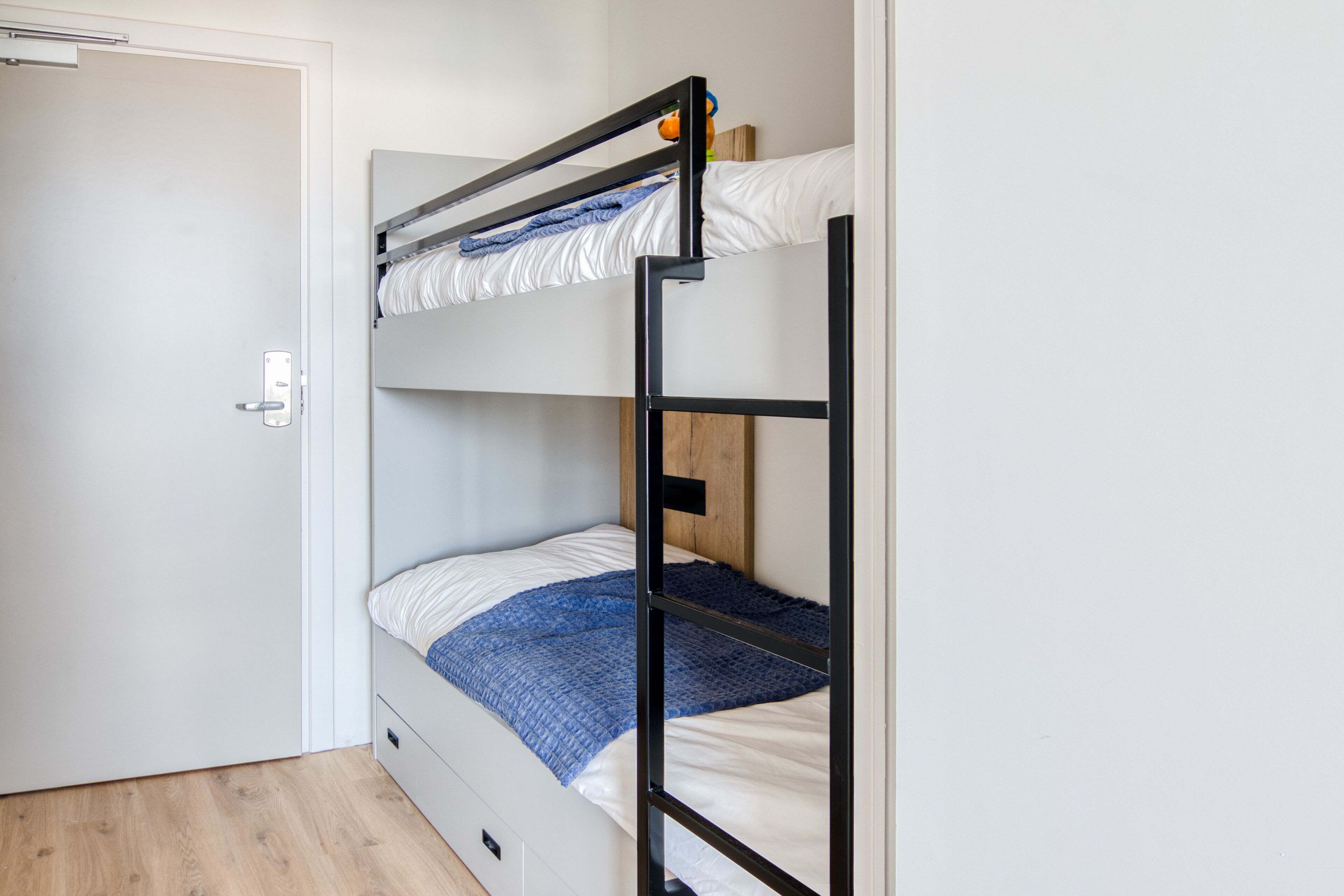A bunk bed with a wooden headboard, a white door, and a light wooden floor.