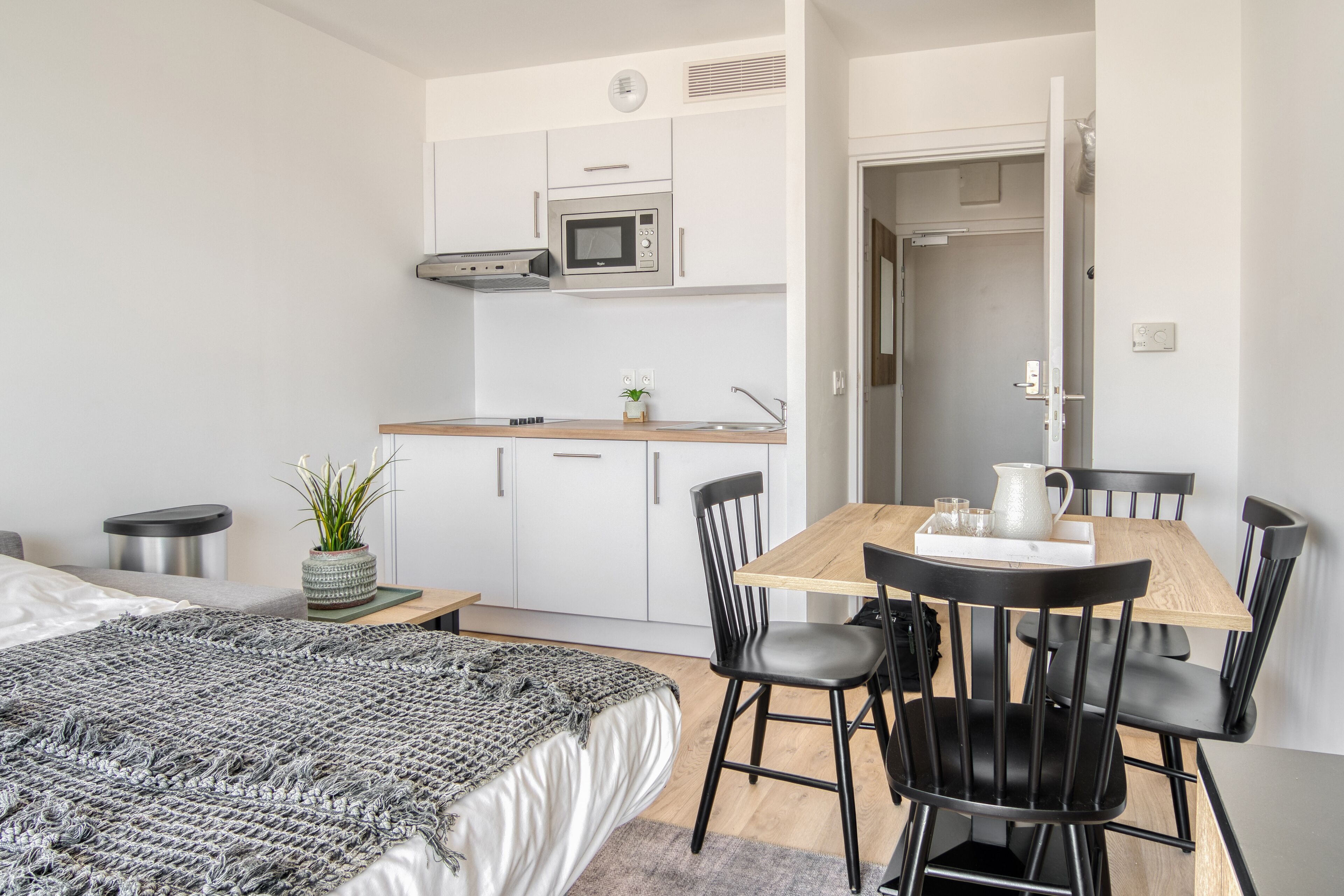 A compact bedroom with a bed, bedside table, and a small desk with a plant.