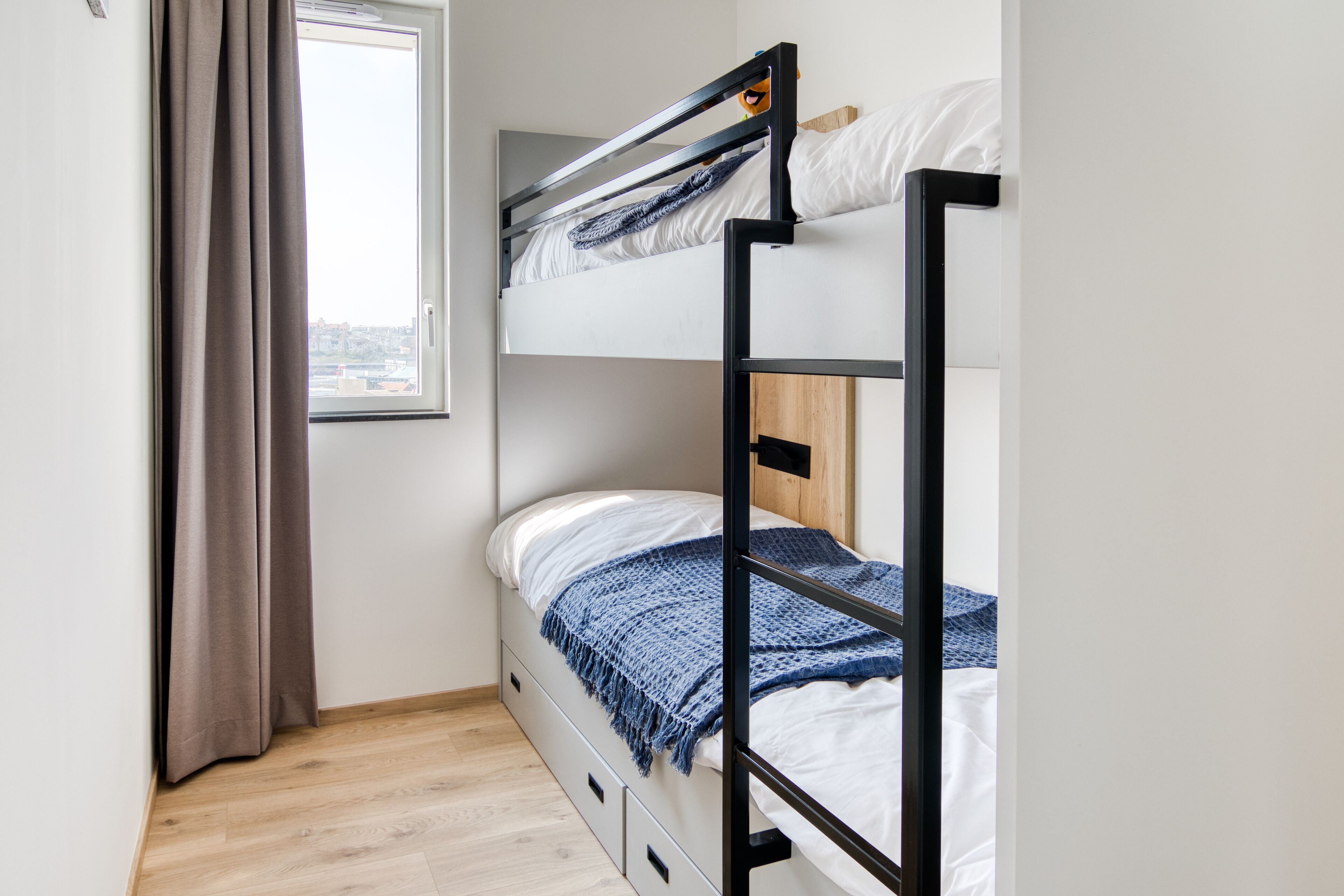 Une chambre avec un lit superposé, une fenêtre, des rideaux et un plancher en bois.