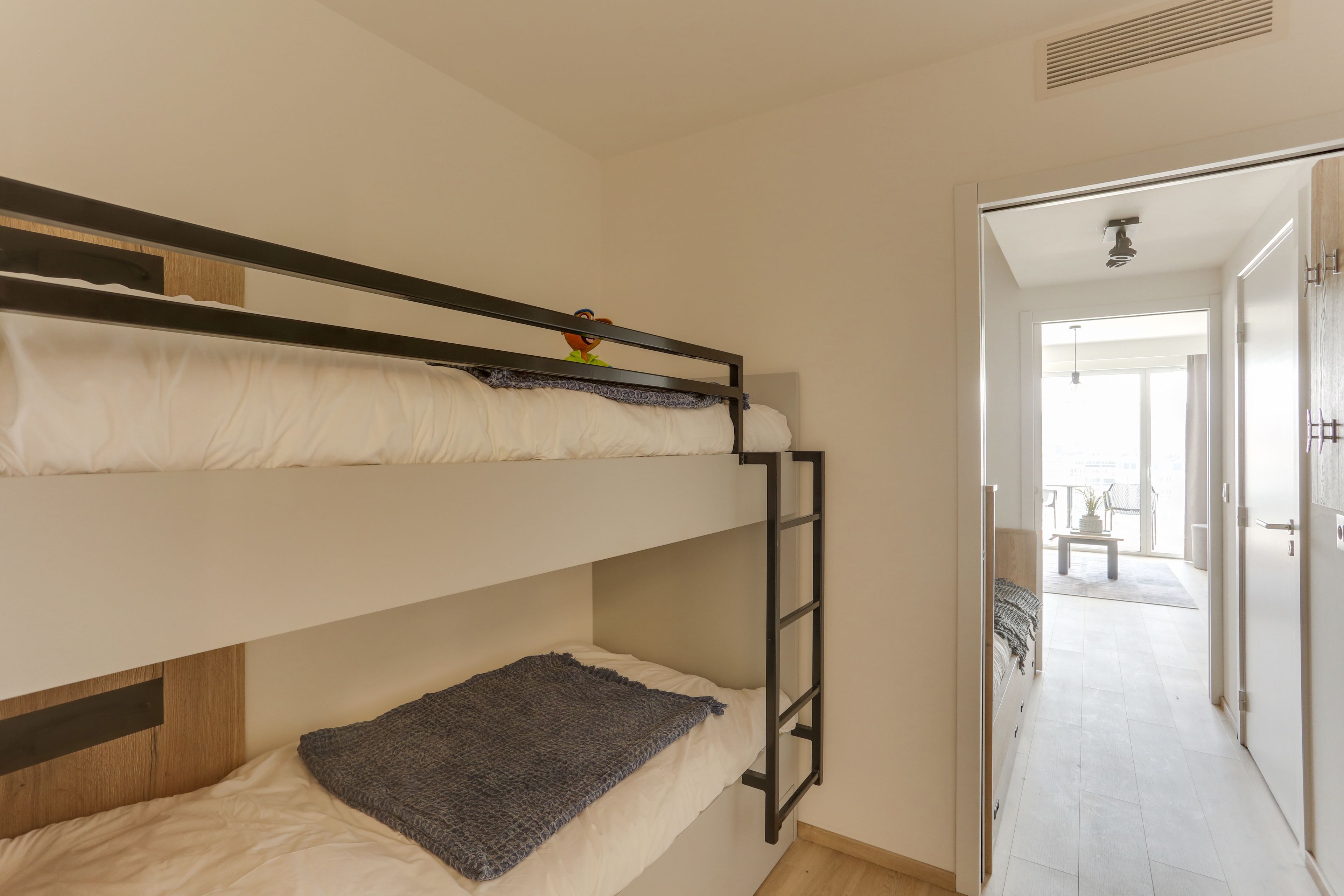 A bunk bed room with a ladder, a small table, and a view of a balcony.