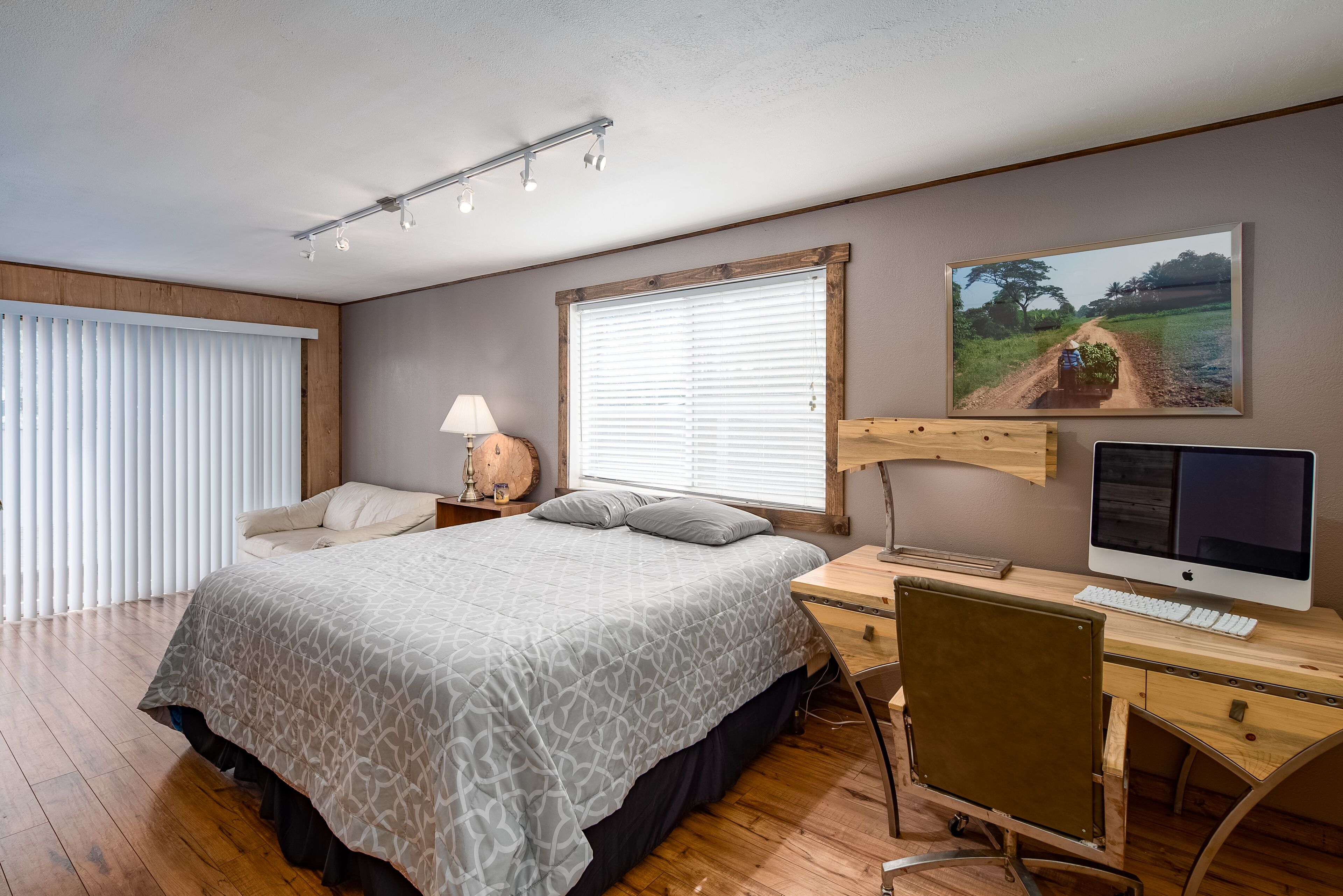 A bedroom with a bed, a desk with a computer, a lamp, and a painting on the wall.