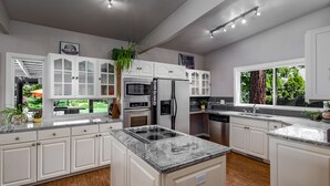 A modern kitchen with white cabinetry, a granite countertop, a built-in stove, and a large window overlooking a garden. - Parkway House - PICKLEBALL COURT- Dog Friendly  - Basketball - FAMILY PERFECT  (Nine Mile Falls)