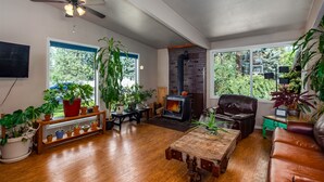 A spacious living room with a fireplace, wooden flooring, leather sofa, and various potted plants. - Parkway House - PICKLEBALL COURT- Dog Friendly  - Basketball - FAMILY PERFECT  (Nine Mile Falls)