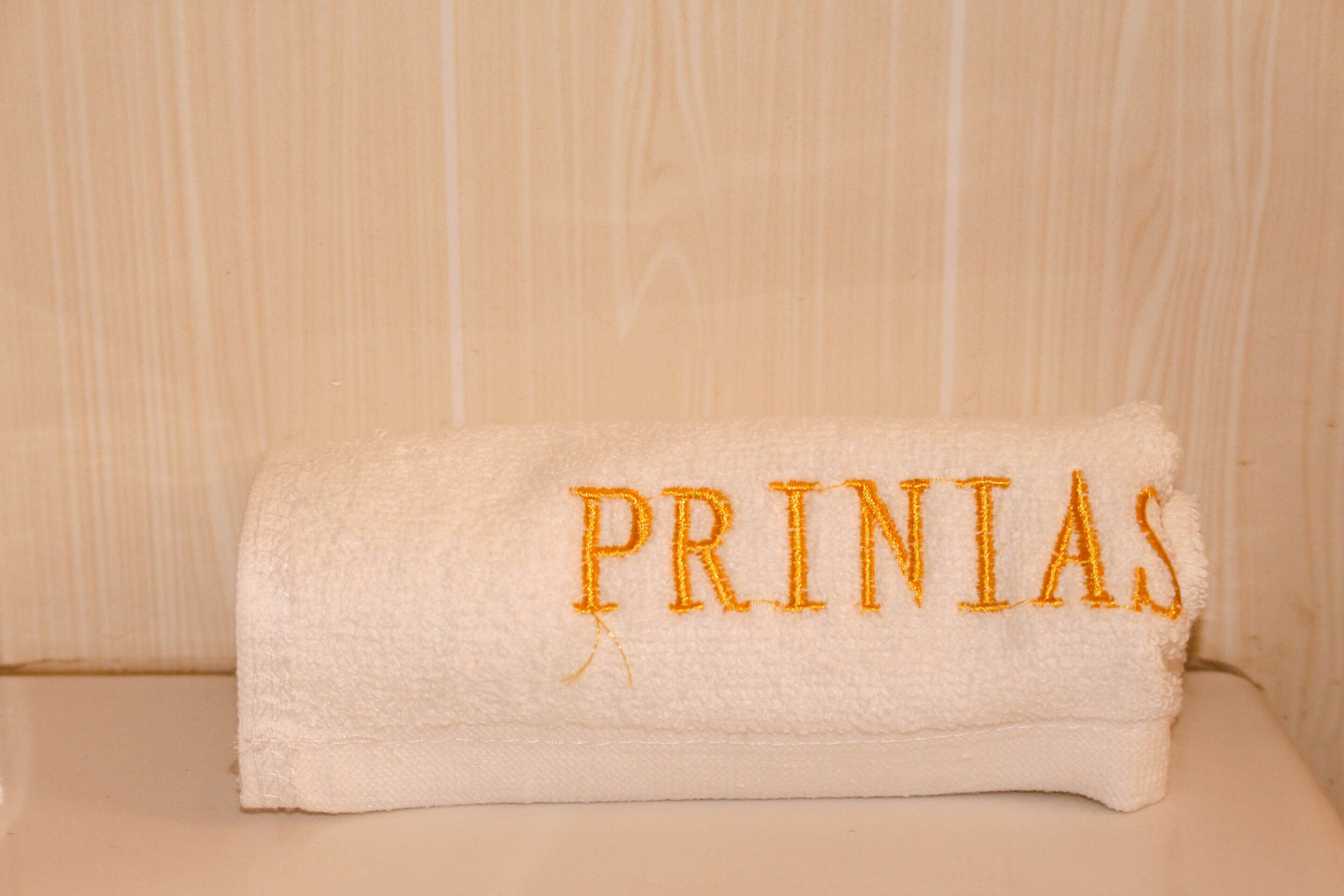 Une serviette blanche avec le texte « PRINIAS » brodé, posée sur une surface en bois.