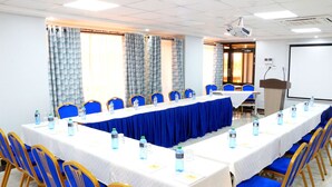 Un salón de conferencias con una larga mesa, sillas azules y botellas de agua.