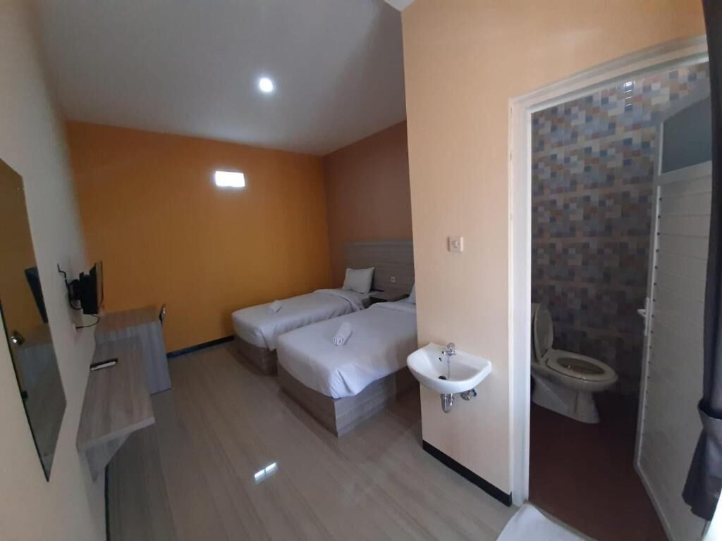 A hotel room with two beds, a sink, and a toilet.