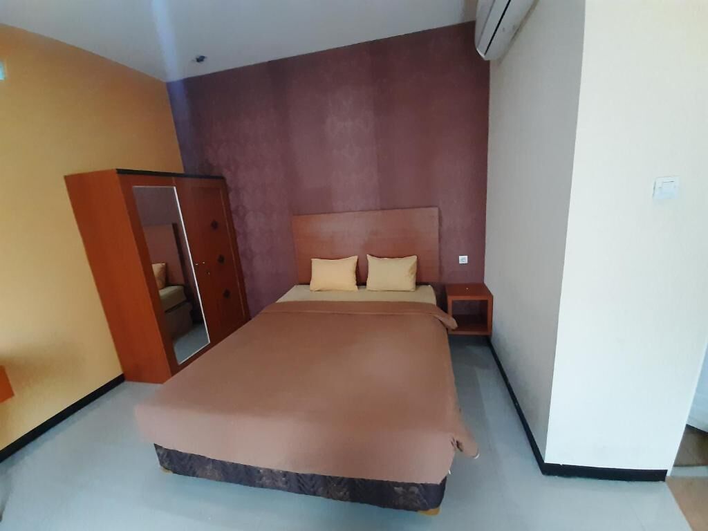 A bedroom with a bed, a nightstand, a wardrobe, and an air conditioning unit.
