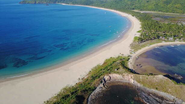 A coastal landscape with a sandy beach, clear blue waters, and lush green hills in the background. - Nacpan Beach Glamping Managed by H Hospitality (El Nido)
