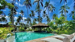 A pool area with lounge chairs, a thatched-roof structure, and tall palm trees. - Nacpan Beach Glamping Managed by H Hospitality (El Nido)