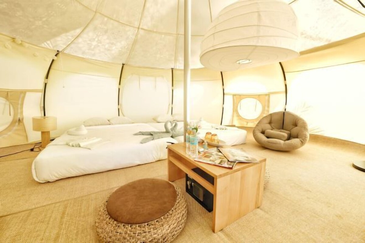A cozy tent-style room with a bed, a wooden table, a reading lamp, and a comfortable chair.