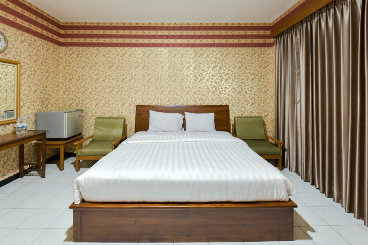 A hotel room with a large bed, two chairs, a desk with a television, and a curtain on the window.
