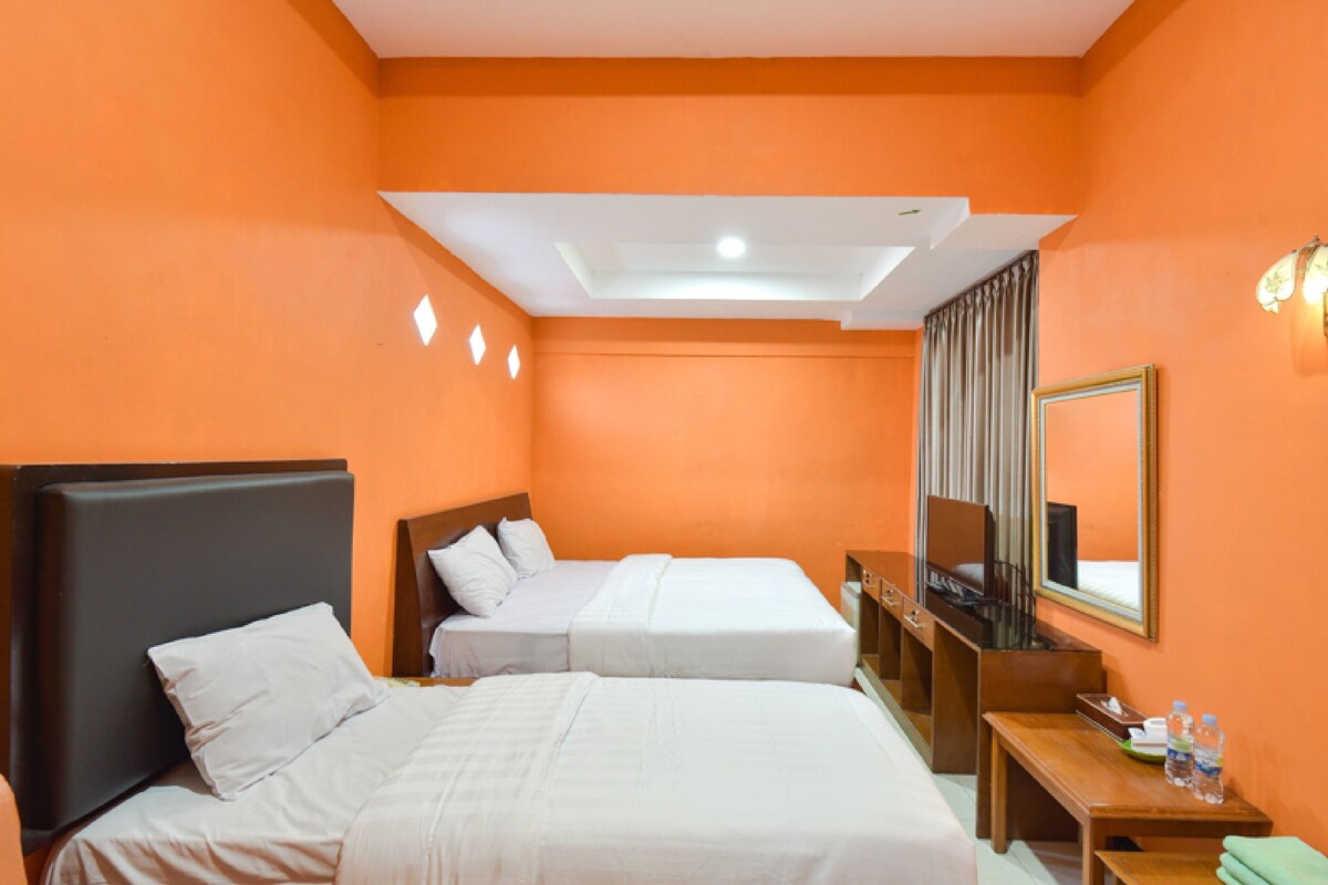 A hotel room with two beds, a wooden desk, a mirror, and a ceiling light.
