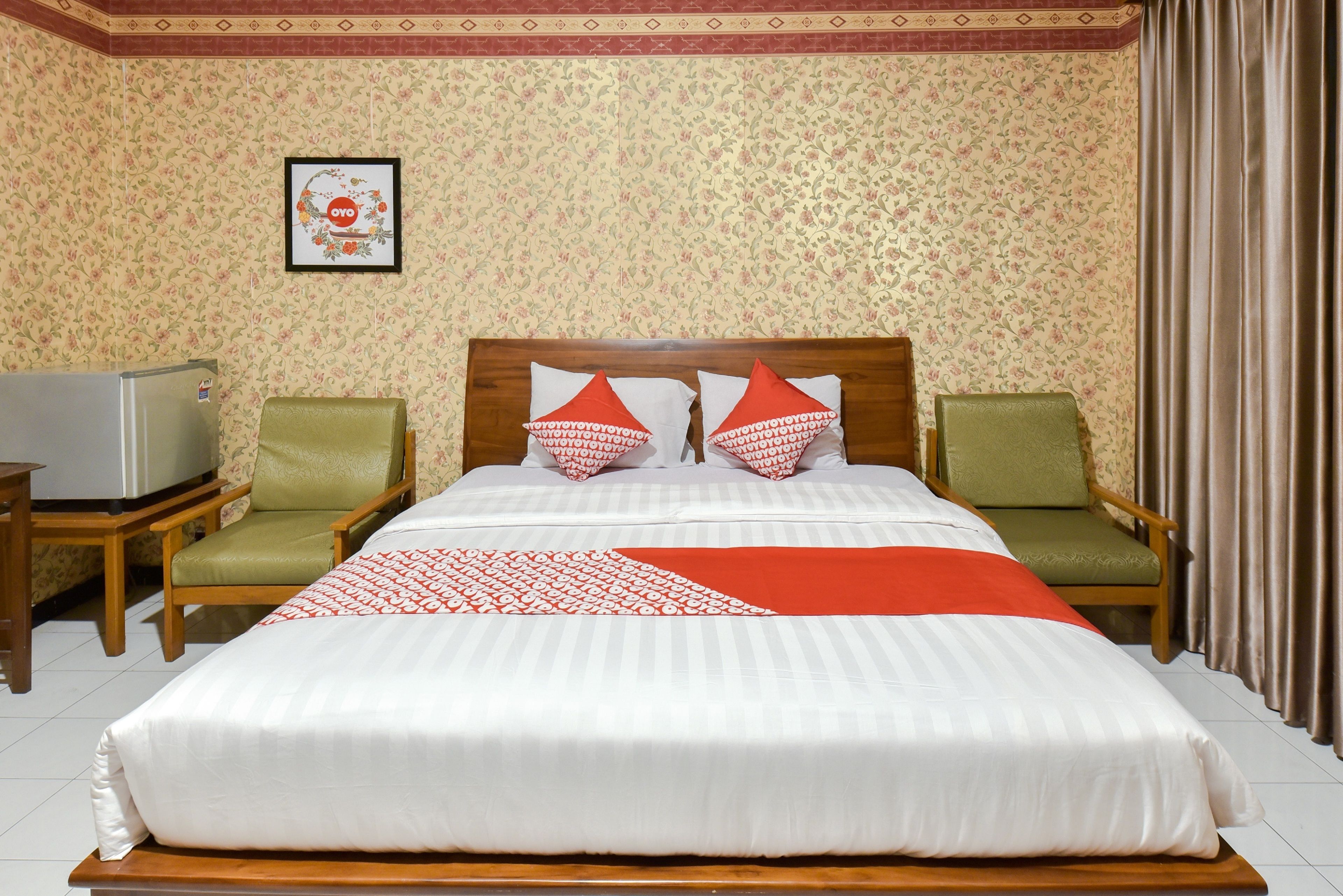 A hotel room with a large bed, two green armchairs, a wooden nightstand, and a television.