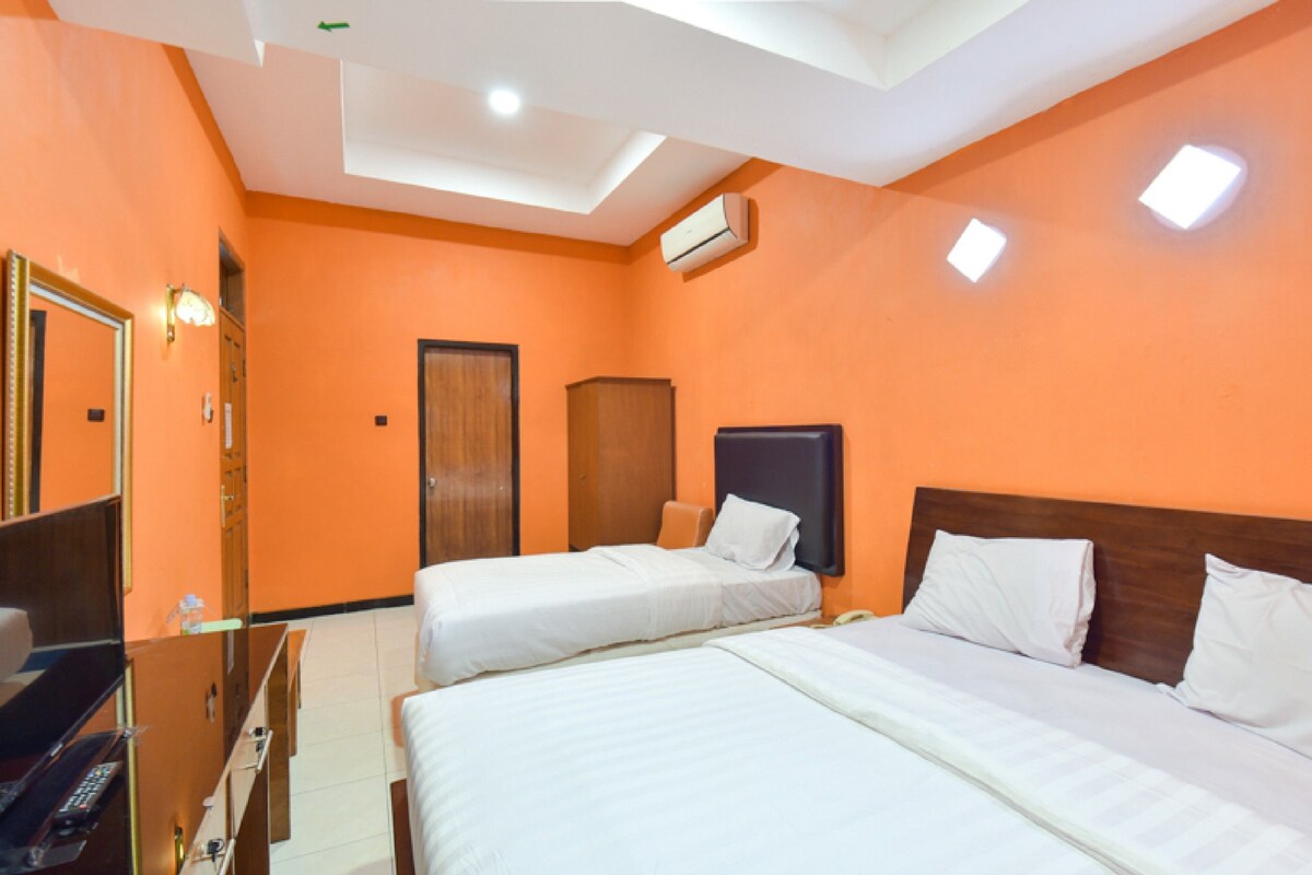 A hotel room with two beds, a desk, and an air conditioning unit.
