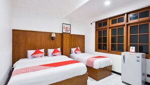 A hotel room with two beds, wooden headboards, white bedding with red accents, a small refrigerator, and a window with wooden frames. - Hotel Sekar Ayu (Yogyakarta)