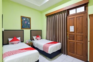 Habitación de hotel con dos camas, una puerta de madera, un cuadro en la pared y una ventana con cortinas.