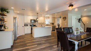Een moderne keuken met witte kastjes, een centraal eiland en een eethoek met een houten tafel en stoelen.