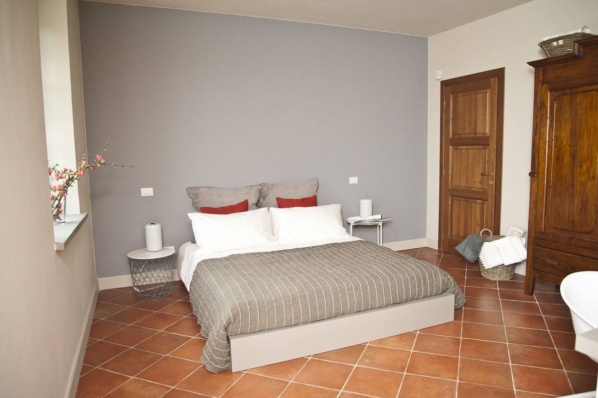 A bedroom with a bed, a nightstand, a bedside table, a wooden wardrobe, and a bathroom with a toilet.