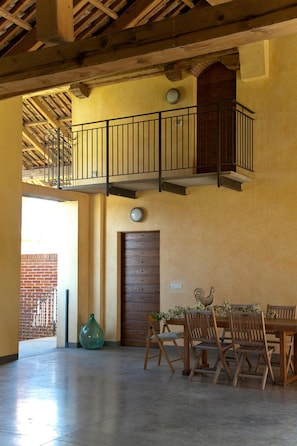 A spacious room with a high ceiling, a wooden staircase, a dining area with wooden chairs and a table, and a large green vase. - Cascina San Giorgio (Valenza)