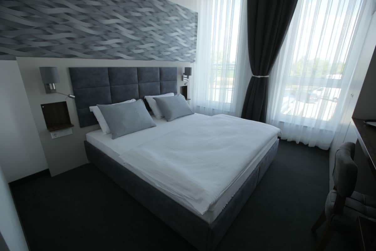 A modern hotel room with a large bed, a headboard with a geometric pattern, a bedside table, and a chair.