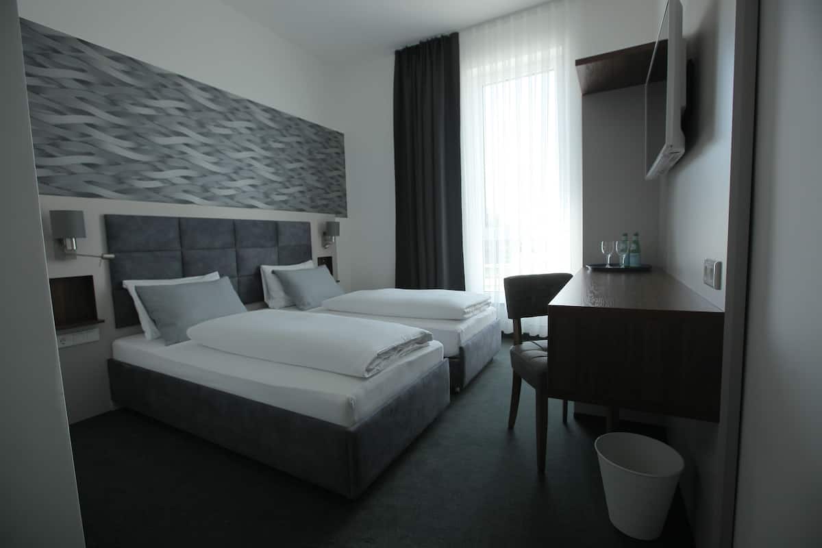 A modern hotel room with two beds, a desk, a chair, a TV, and a bathroom.