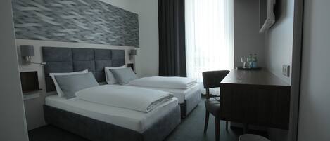 A modern hotel room with two beds, a desk, a chair, a TV, and a bathroom.