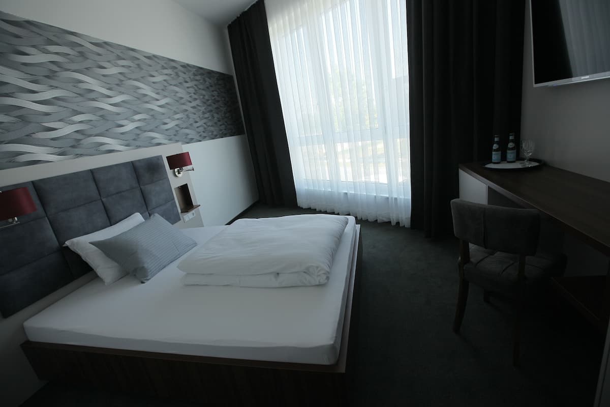 A hotel room with a large bed, a desk with a chair, a TV, and a window with curtains.