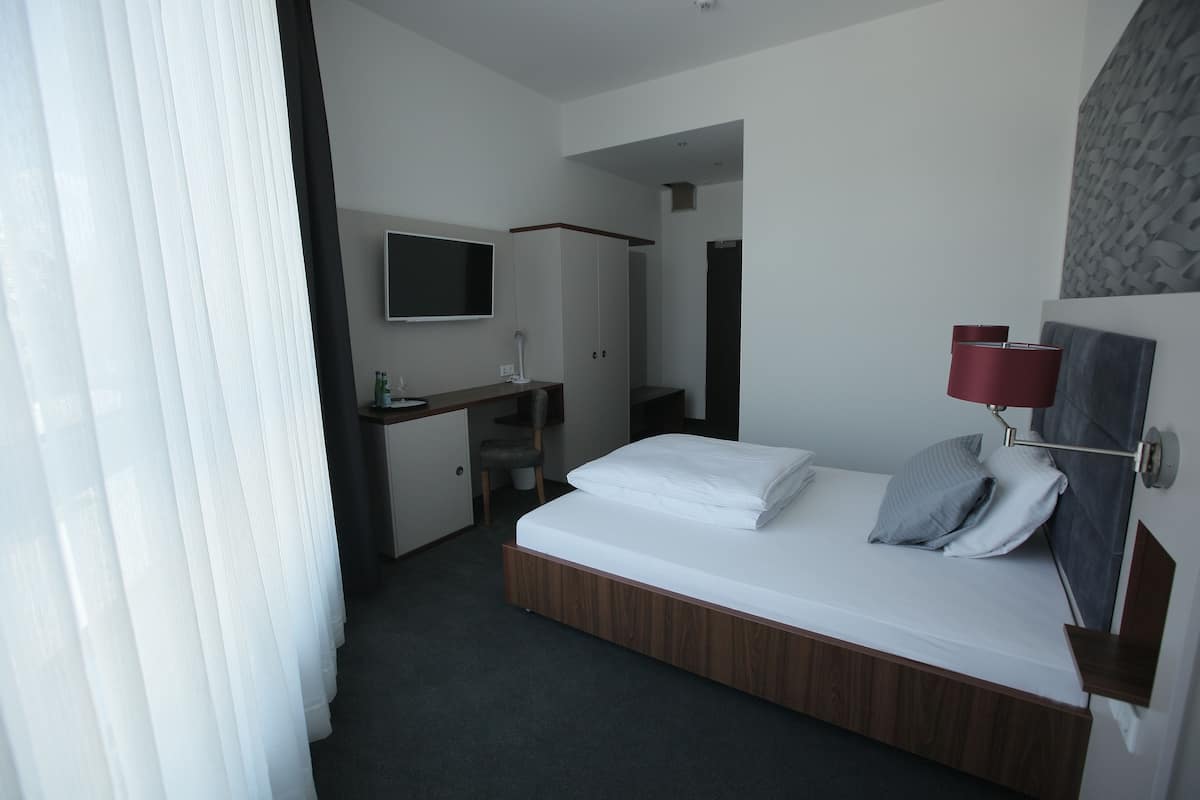 A modern hotel room with a bed, a desk, a chair, a TV, and a red lamp.