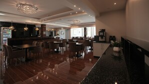 A spacious dining area with multiple tables and chairs, a bar area with a Coca-Cola refrigerator, and a modern chandelier. - Hotel Starton am Ingolstadt Village (Ingolstadt)