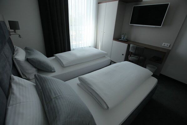 A hotel room with two beds, a TV, a wardrobe, and a desk with a chair.