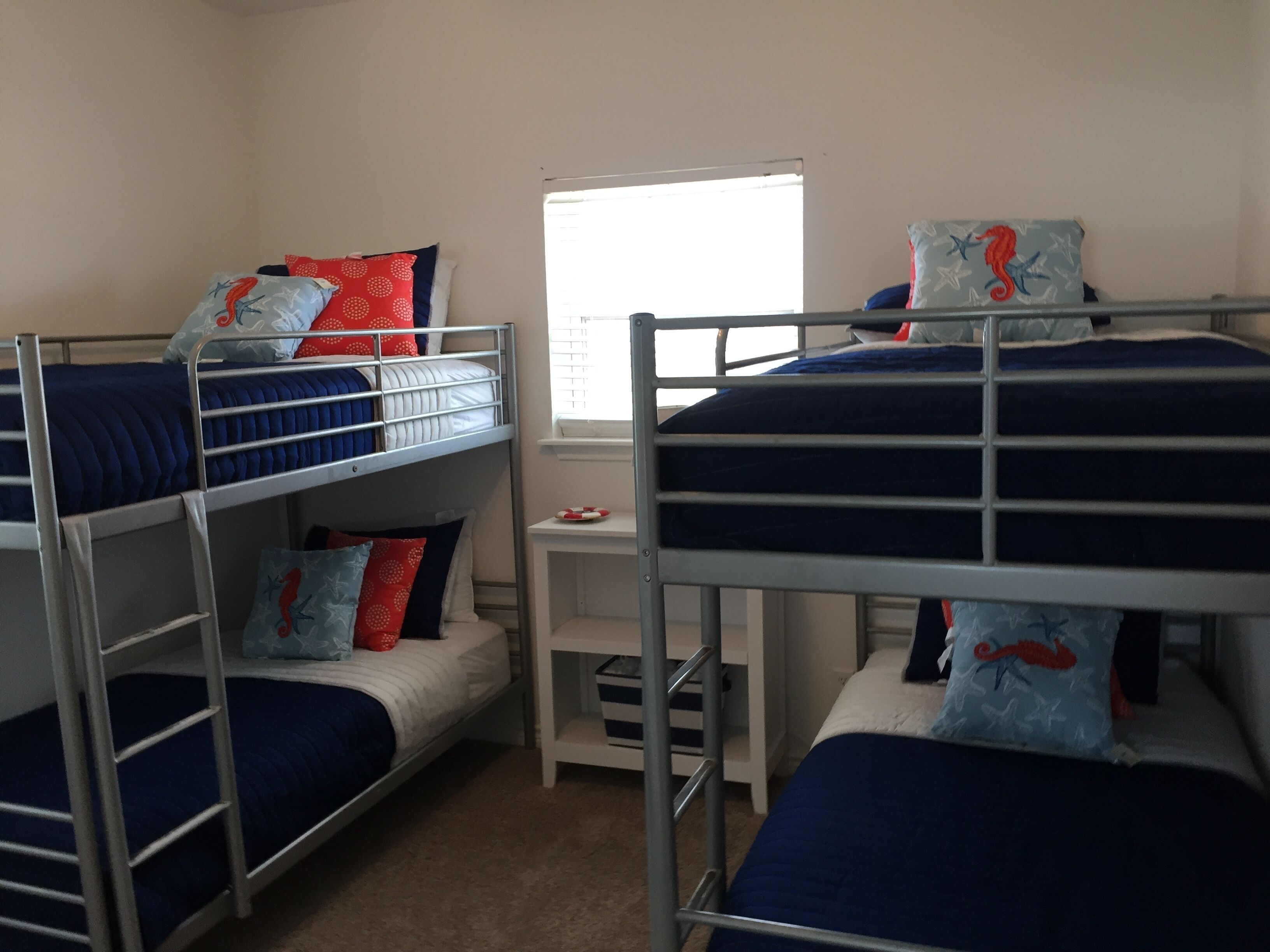 A dormitory room with bunk beds, a small desk, and a window.