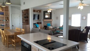 Een ruime keuken met een centraal eiland, houten kasten en een inbouwoven. Er is een zithoek met een tafel en stoelen, en een woonkamer met banken en een televisie.