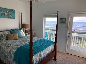 A bedroom with a four-poster bed, a view of the ocean through a door, and a painting of a sea turtle on the wall. - Beachfront Surfside Home Gulf Views, Wraparound Decks, King + Bunks, Sleeps 12 (Freeport)