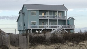 Een twee verdiepingen tellend strandhuis met een balkon en een klein aangebouwd gedeelte.