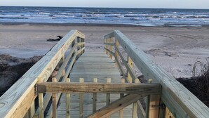 Een houten looppad dat naar een strand leidt, met golven op de achtergrond.