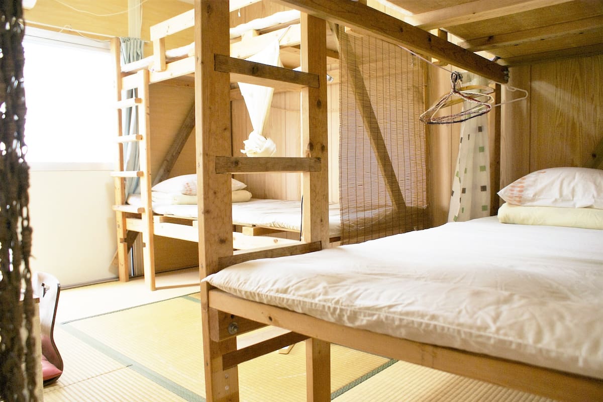 Une pièce de style japonais traditionnel, avec un sol recouvert de tatamis, un lit superposé, un bureau en bois et un portant à vêtements.