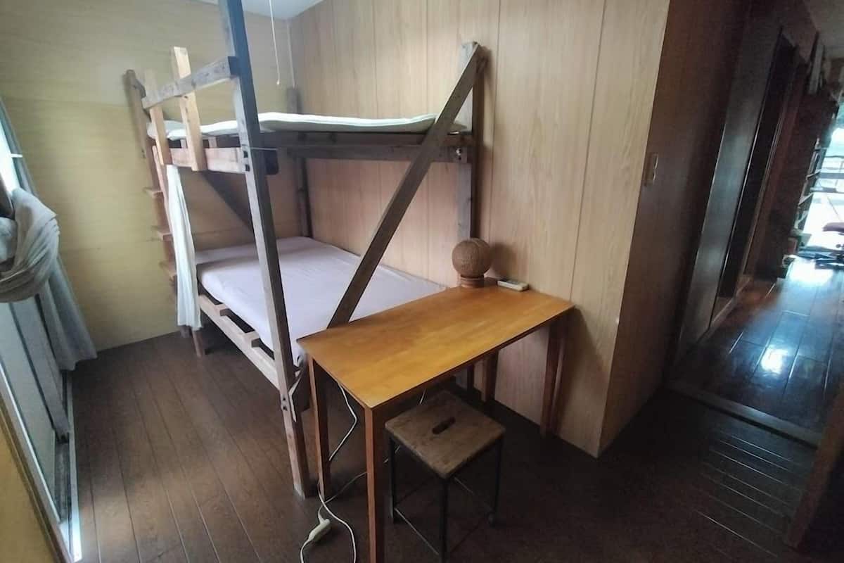 Un lit superposé avec une table en bois et un petit tabouret, dans une pièce aux murs et au plancher en bois.