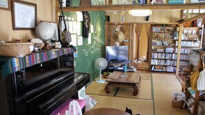 Una sala de estar acogedora con un piano, una estantería, un ventilador y un gato.