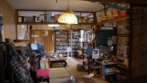 Una habitación tradicional japonesa con suelo de tatami, un televisor, una estantería y una lámpara colgante.