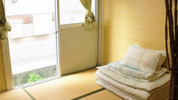 A room with tatami flooring, a bed with a white mattress and pillow, an air conditioning unit, and a sliding door with a view of the outside.