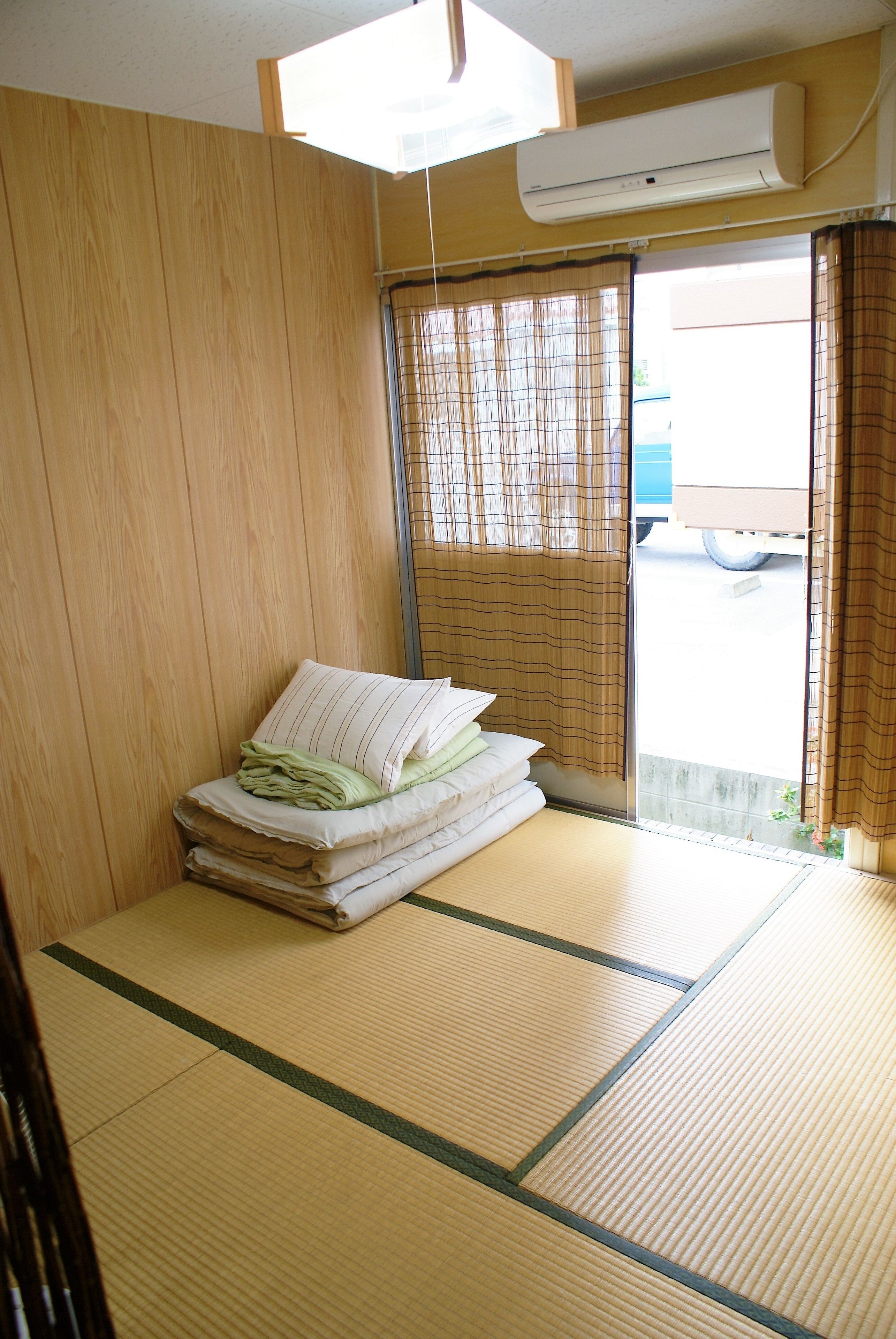 A room with tatami flooring, a bed with pillows, a sliding door, and an air conditioning unit.