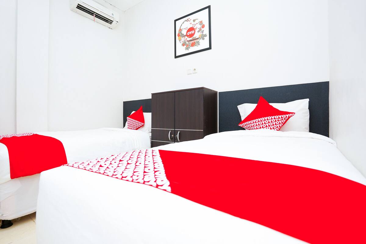 A hotel room with two beds, a dark wooden wardrobe, and a framed picture on the wall.